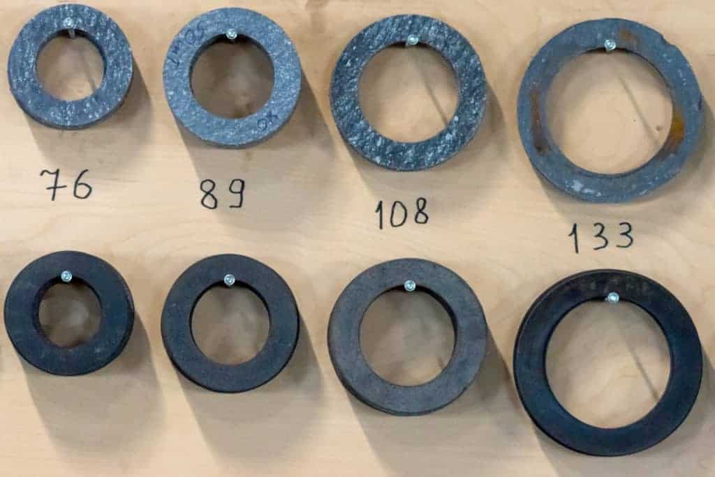 Flat metal gaskets of various dimensions stacked against a wall. 
