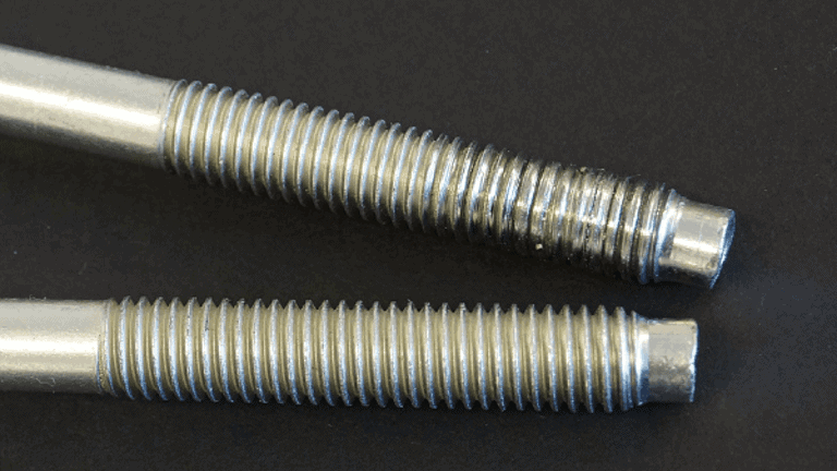 Two threaded bolts lay side-by-side. The top shows signs of galling, where parts of the thread have worn off.