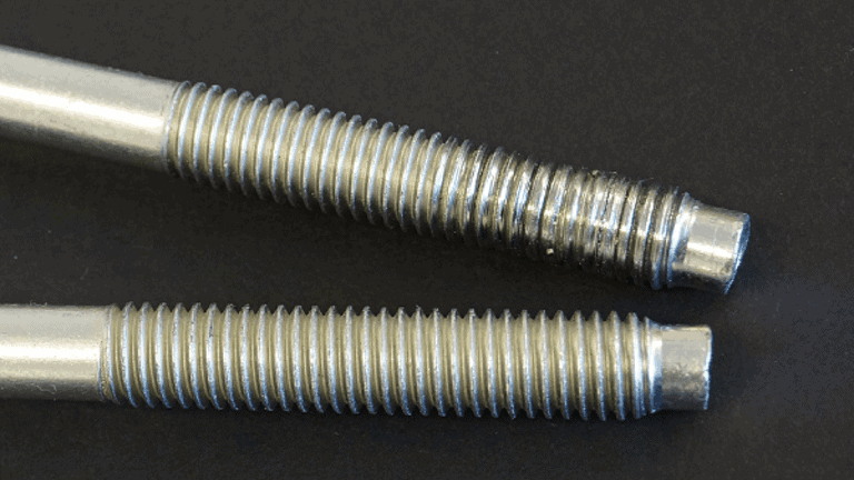 Two threaded bolts lay side-by-side. The top shows signs of galling, where parts of the thread have worn off. 